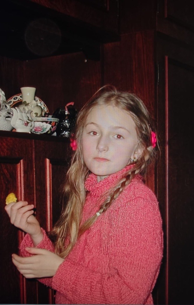 Patrycja as a child in a pink sweater with long braided hair